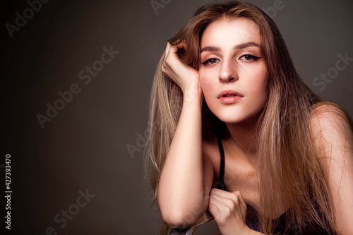 Natural Sensual Portrait of Charming Caucasian Blond Girl With Long Beautiful Hair Posing in Studio Against Dark Background.