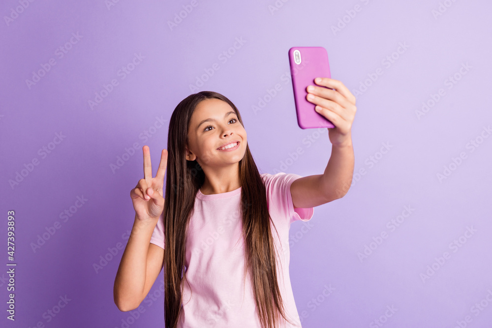 Photo of charming cute schoolgirl dressed t-shirt tacking selfie modern device showing v-sign isolated purple color background Photo of charming cute schoolgirl dressed t-shirt tacking selfie modern device showing v-sign isolated purple color background