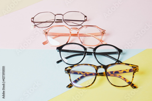 multiple eyeglasses on a multicolored background of pastel colors, geometric background, pink yellow and light blue colors, trendy eyeglass frames