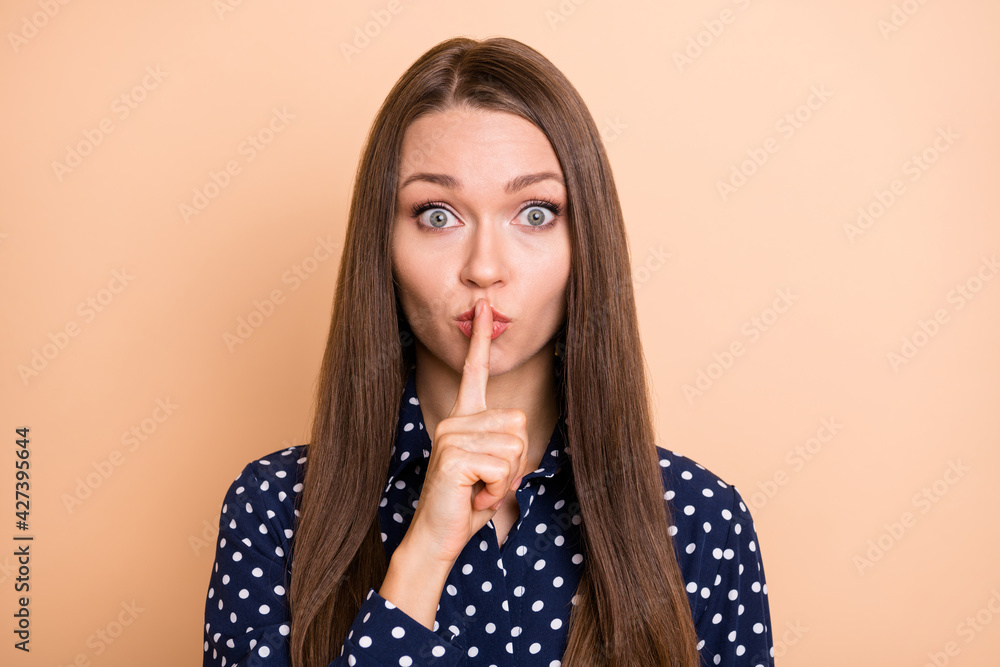 Photo of impressed cute young girl dressed dotted blouse finger lips ask not tell secrets isolated beige color background Photo of impressed cute young girl dressed dotted blouse finger lips ask not tell secrets isolated beige color background