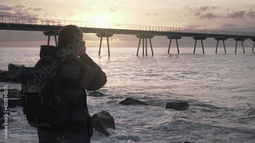 Travel Photographer wearing backpack taking pictures of the sunrise and seascape at the beach