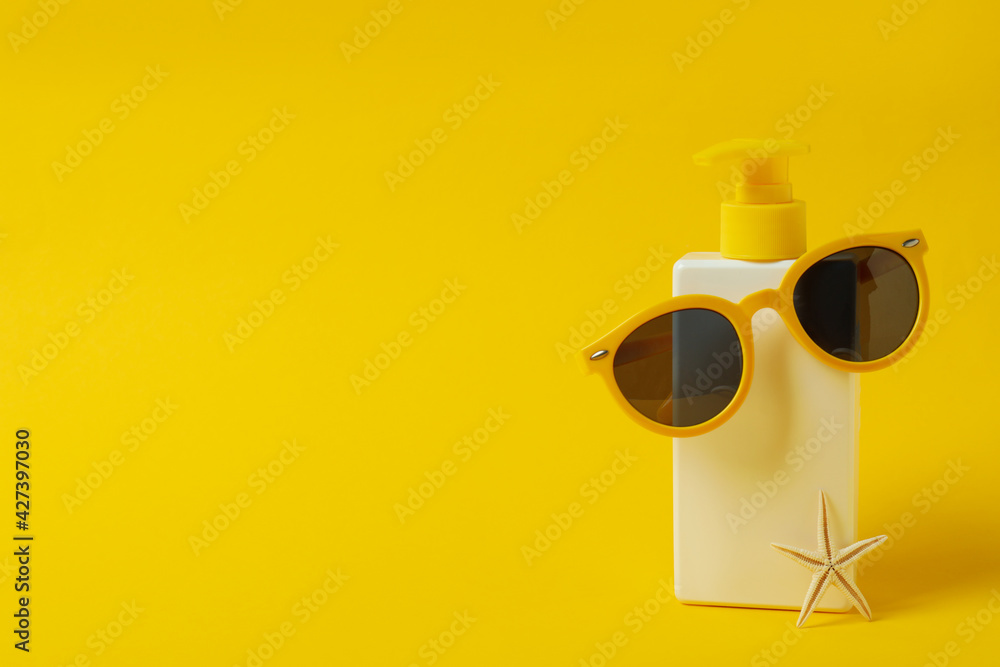 Bottle of sunscreen with sunglasses and starfish on yellow background Bottle of sunscreen with sunglasses and starfish on yellow background