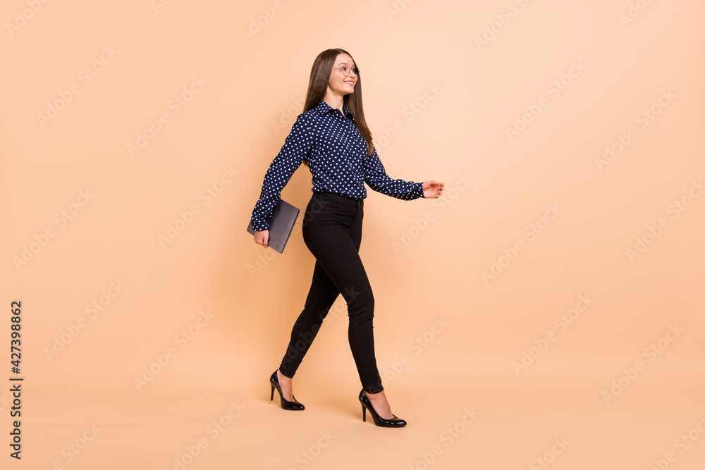 Photo of pretty shiny young girl dressed dotted blouse glasses holding modern device walking isolated beige color background Photo of pretty shiny young girl dressed dotted blouse glasses holding modern device walking isolated beige color background