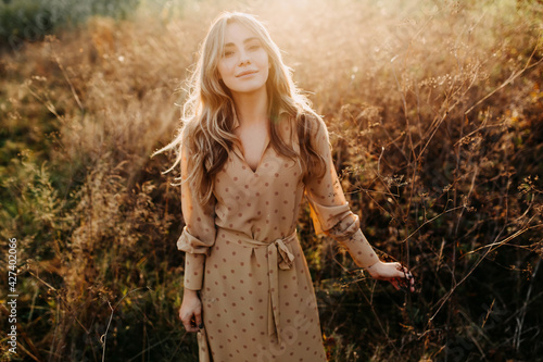 Young woman with long blonde wavy hair, walking in a field with tall dry grass, smiling. © Bostan Natalia