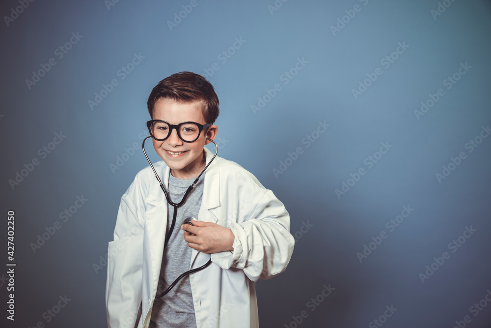 cool young boy is disguised as a doctor with a white doctor smock and plays with syringe and stethoscope in front of blue background in the studio cool young boy is disguised as a doctor with a white doctor smock and plays with syringe and stethoscope in front of blue background in the studio