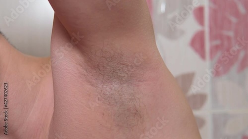 young caucasian man in the bathroom trimming the hair of his armpit with an electric trimmer