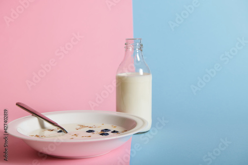 A healthy breakfast with fresh milk and a plate of oatmeal and blueberries, isolated on bicolor pink and blue background