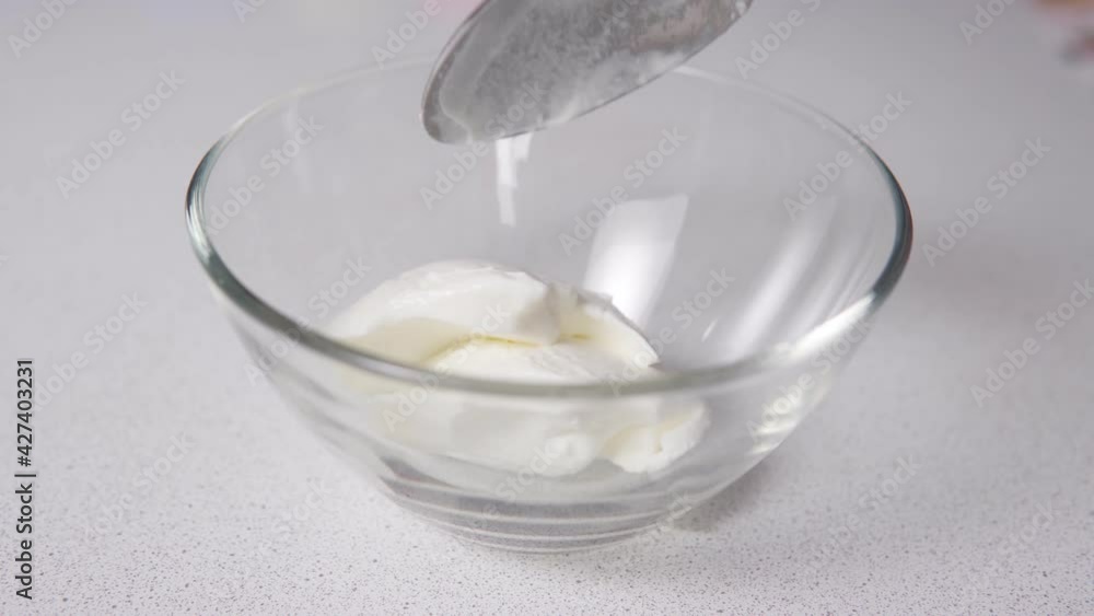 Sour cream is poured with a spoon into a transparent bowl. Cooking food Sour cream is poured with a spoon into a transparent bowl. Cooking food