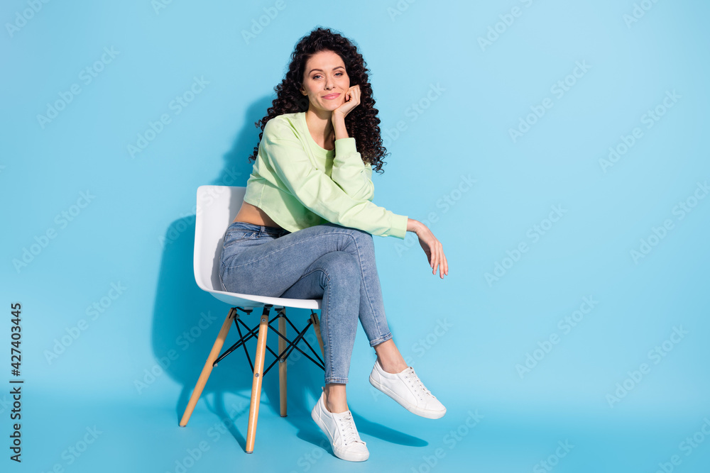 Photo of charming girl sit chair fist cheek look camera wear sweatshirt jeans footwear isolated blue background Photo of charming girl sit chair fist cheek look camera wear sweatshirt jeans footwear isolated blue background