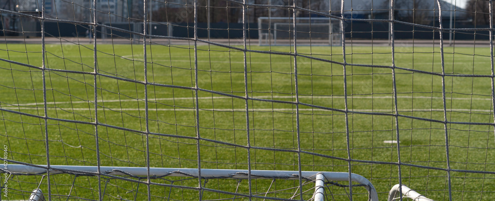 Fototapeta premium View through the net of a soccer goal, football gate. Green synthetic grass sports field with white line shot. Sports background.