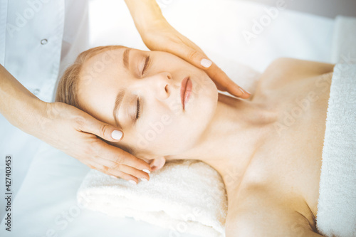 Happy woman enjoying facial massage with closed eyes in spa salon. Relaxing treatment in medicine and Beauty concept