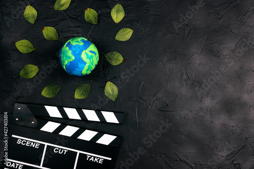 Movie clapper board and globe surrounded by leaves on black background. photo
