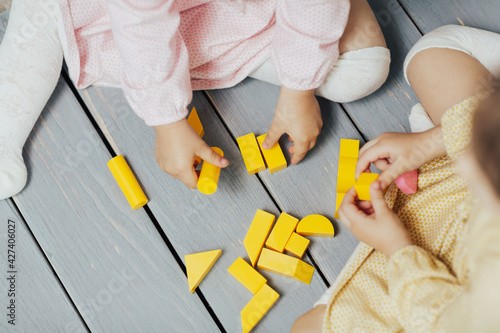 Top view on children's hands playing with colourful yellow blocks on the wooden table background. Learning and education concept. 