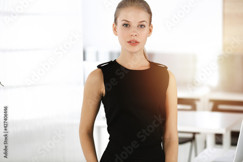 Free Download Young blond businesswoman dressed in black dress looks perfect in sunny modern office. Business people concept - GFXLoad