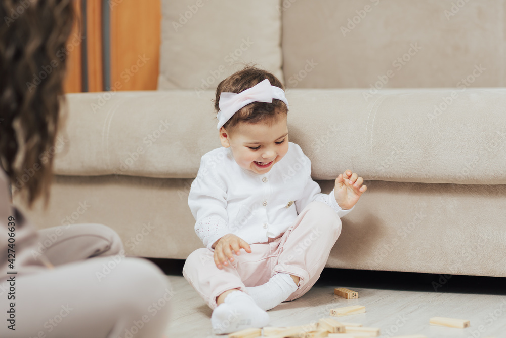 Fototapeta premium Smiling baby play with his mother on warm floor with wooden blocks at home.