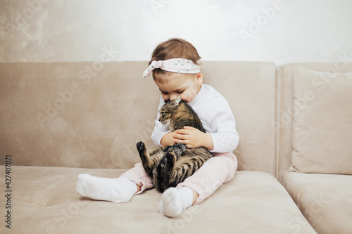 Child girl hug and kiss the his cute funny cat with tenderness and love while sitting on the sofa in the living room. © eduard