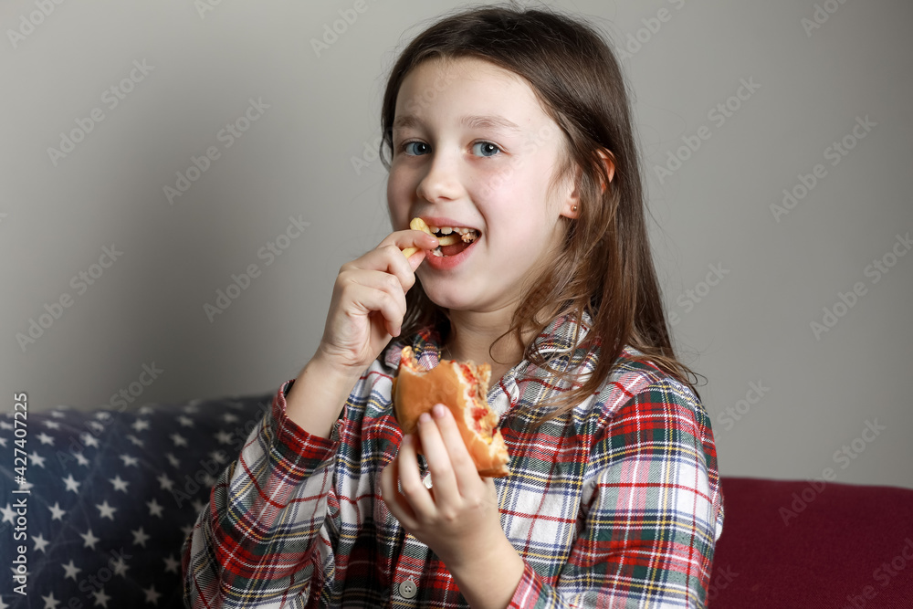 a cute little girl emotionally eating a hamburger, sandwich, cheeseburger or burger and smiling at home a cute little girl emotionally eating a hamburger, sandwich, cheeseburger or burger and smiling at home