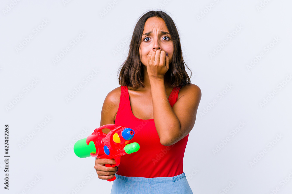Young mixed race woman holding a water gun isolated biting fingernails, nervous and very anxious. Young mixed race woman holding a water gun isolated biting fingernails, nervous and very anxious.