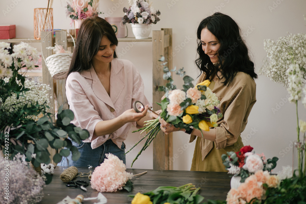 Two young women florist working in flower studio, making beautiful bouquet using fresh plants and flowers.