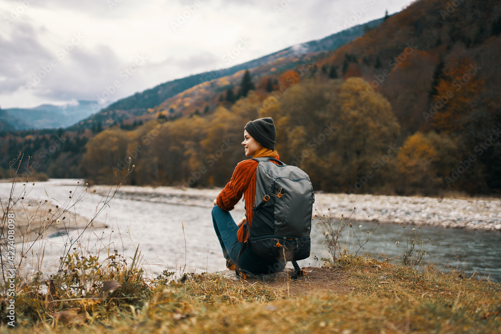 woman sits on the grass in the mountains near the river and autumn landscape