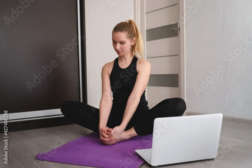 young woman doing asana at home on yoga mat in front of laptop