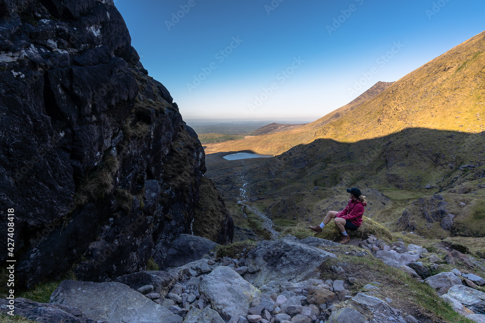 woman sitting looking at landscape on hilly road with lake in background in kerry mountains
