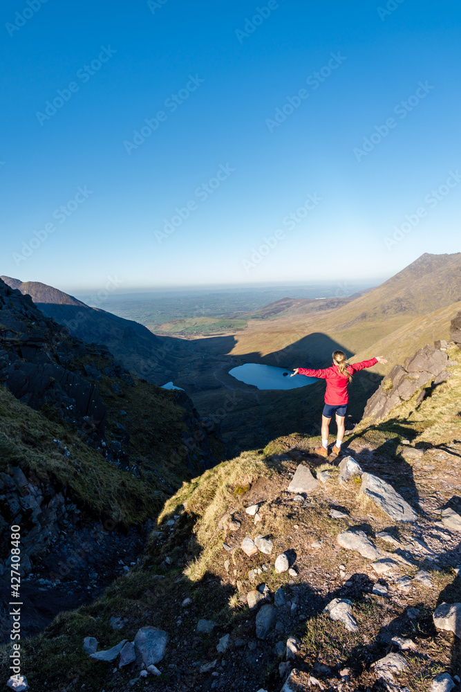 happy woman raising her arms on top of devils ladder with two lakes in background on Carrantuohill mountain