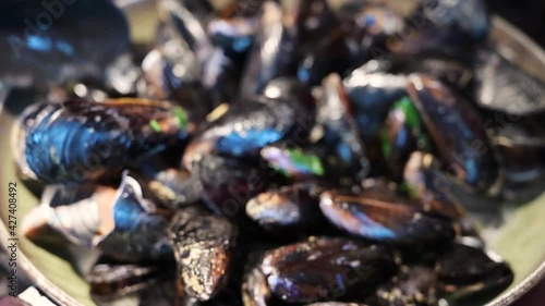 Close up shot of a mussel on a black kitchen spoon. In the background the pot where they are cooking: you can see the steam rising and the cooking broth boiling.The spoon mix it. Mediterranean cuisine photo