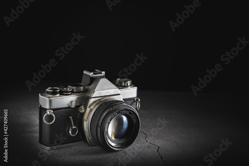 Dark product photography of a old film retro camera with shallow depth of field on a stone background. Camera technology concept with a vintage look with copy space.