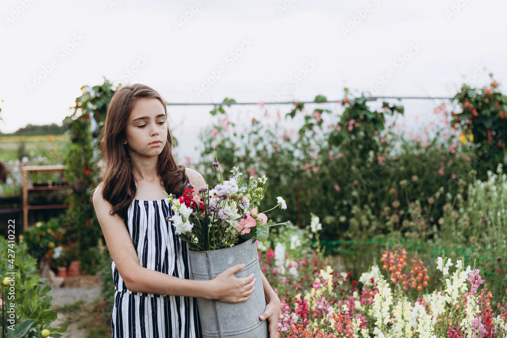 pretty girl with a bucket with different wildflowers posing for a photo on the territory of a flower greenhouse