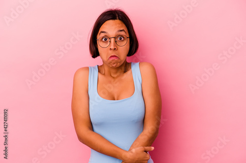 Young mixed race woman isolated on pink background shrugs shoulders and open eyes confused.