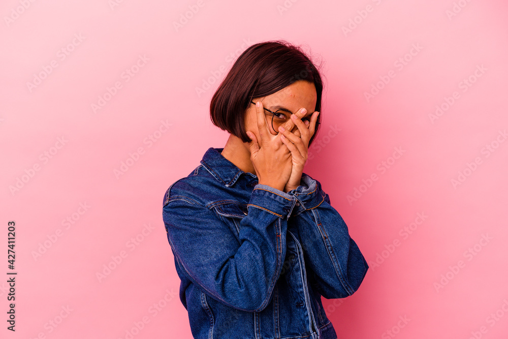 Young mixed race woman isolated on pink background blink through fingers frightened and nervous. Young mixed race woman isolated on pink background blink through fingers frightened and nervous.