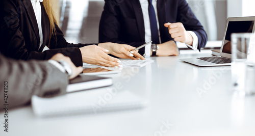 Unknown businessmen and woman sitting, working and discussing questions at meeting in modern office, close-up