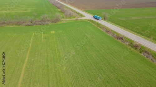 Two large trucks with cargo trailers for loading grain wheat and barley driving along paved road. Concept of goods delivery by automobile. Long endless highway between agronomic fields with crops