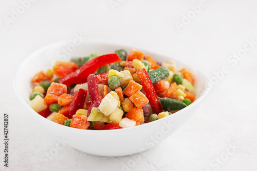 Frozen bell peppers, carrots, corn, peas, celery, onions and tomatoes in a white plate.