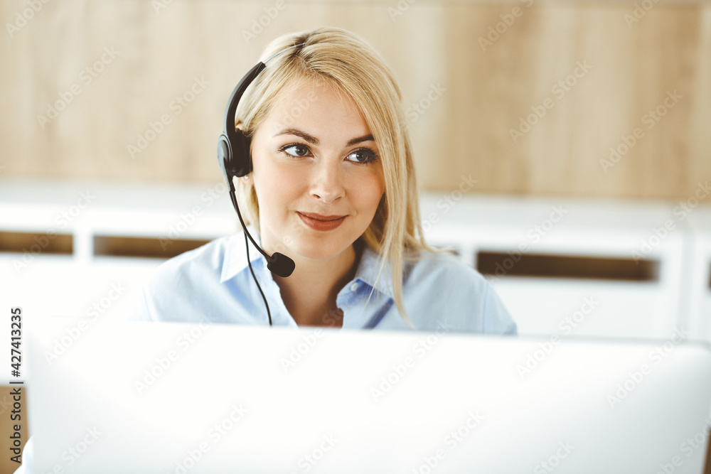 Blonde business woman sitting and communicated by headset in call center office. Concept of telesales business or home office occupation Blonde business woman sitting and communicated by headset in call center office. Concept of telesales business or home office occupation