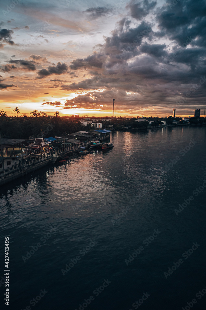 Panorama Cityscape at sunset with large river at foreground and strom clouds at background in Thailand.