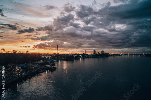 Panorama Cityscape at sunset with large river at foreground and strom clouds at background in Thailand. © Parichart