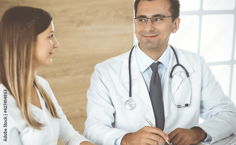 Doctor and patient discussing medical exam results while sitting at the desk in clinic. Male physician using clipboard for filling up medication history record of young woman. Data in medicine Doctor and patient discussing medical exam results while sitting at the desk in clinic. Male physician using clipboard for filling up medication history record of young woman. Data in medicine