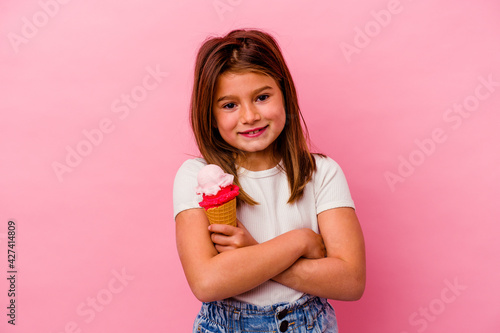 Little caucasian girl holding ice cream isolated on pink background laughing and having fun.