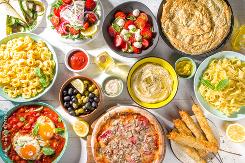 Set of different Mediterranean foods: olives, mozzarella and tomato salad, Greek salad, pasta, tortellini ravioli, pizza, pita lavash sandwich, shish kebab, shakshuka, hummus, top view