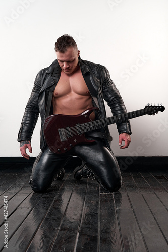 athletic brutal man in a black jacket poses with a guitar in studio              