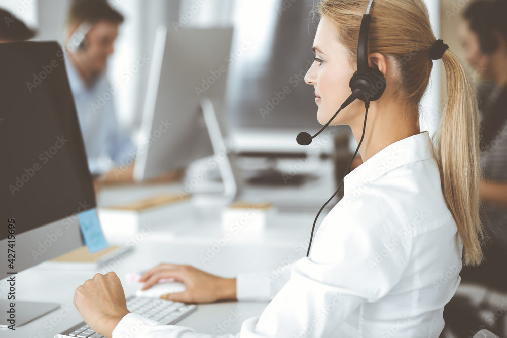 Blonde business woman using headset for communication and consulting people at customer service office. Call center. Group of operators at work Blonde business woman using headset for communication and consulting people at customer service office. Call center. Group of operators at work