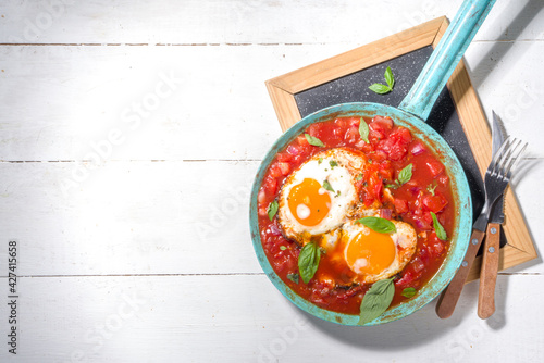 Fototapeta Naklejka Na Ścianę i Meble -  Traditional greek food, Shakshouka. eggs poached in frying pan with tomatoes, olive oil, peppers, onion, garlic, Mediterranean cuisine. Keto, fodmap low carb diet recipe, white wooden background