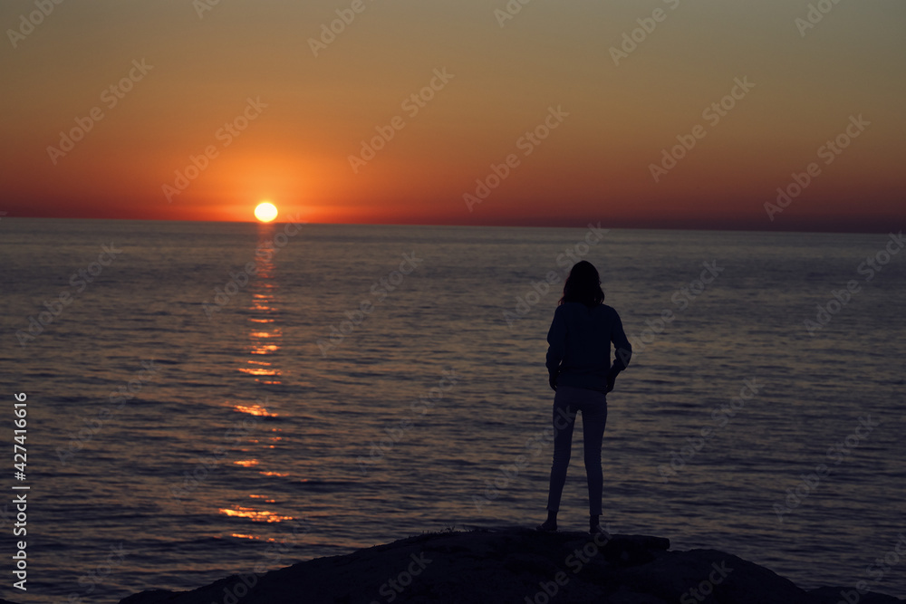 Fototapeta premium sunset in the mountains by the sea and a female silhouette on the beach
