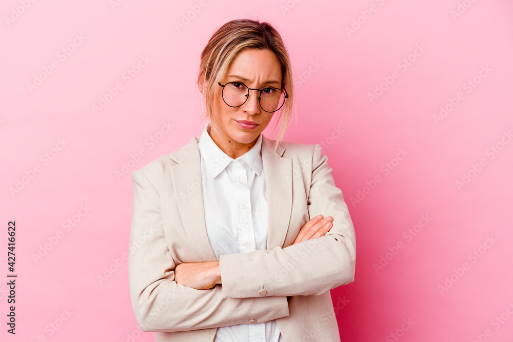 Young caucasian mixed race business woman isolated on pink background frowning face in displeasure, keeps arms folded.