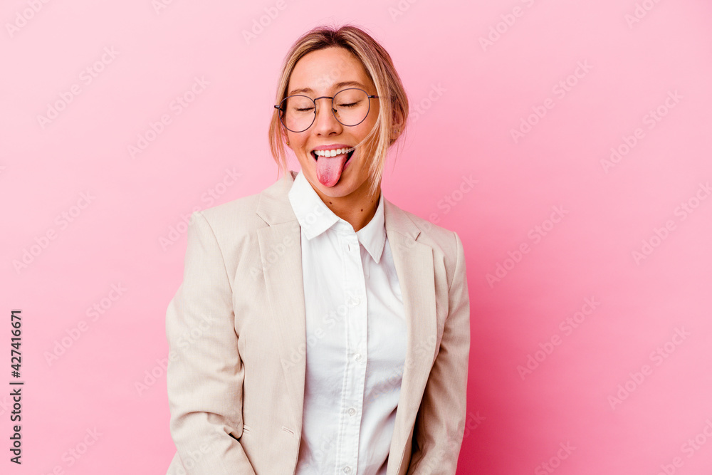 Young caucasian mixed race business woman isolated on pink background funny and friendly sticking out tongue.