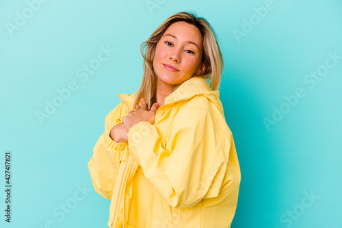 Young mixed race woman isolated on blue background has friendly expression, pressing palm to chest. Love concept. © Asier