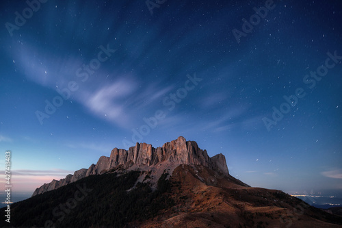 twilight panoramic mountain view, starry sky and clouds, city lights in the background