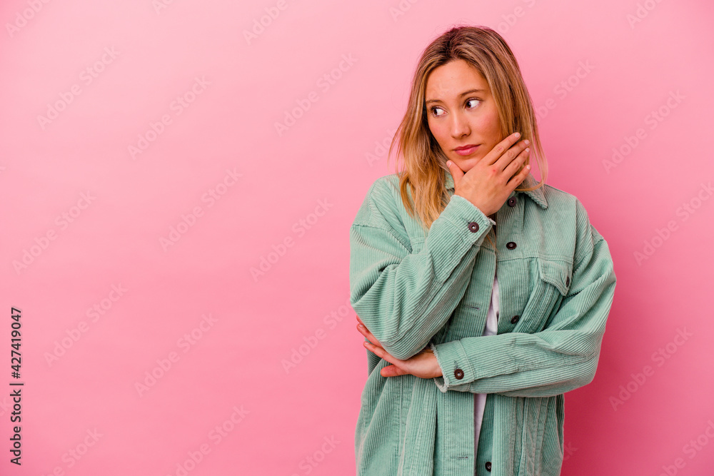 Young mixed race woman isolated on pink background thoughtful looking to a copy space covering mouth with hand. Young mixed race woman isolated on pink background thoughtful looking to a copy space covering mouth with hand.